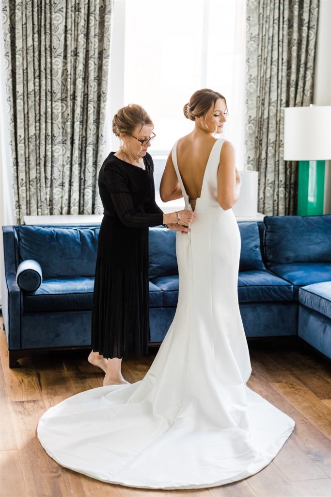 Brides mother fastens her wedding gown