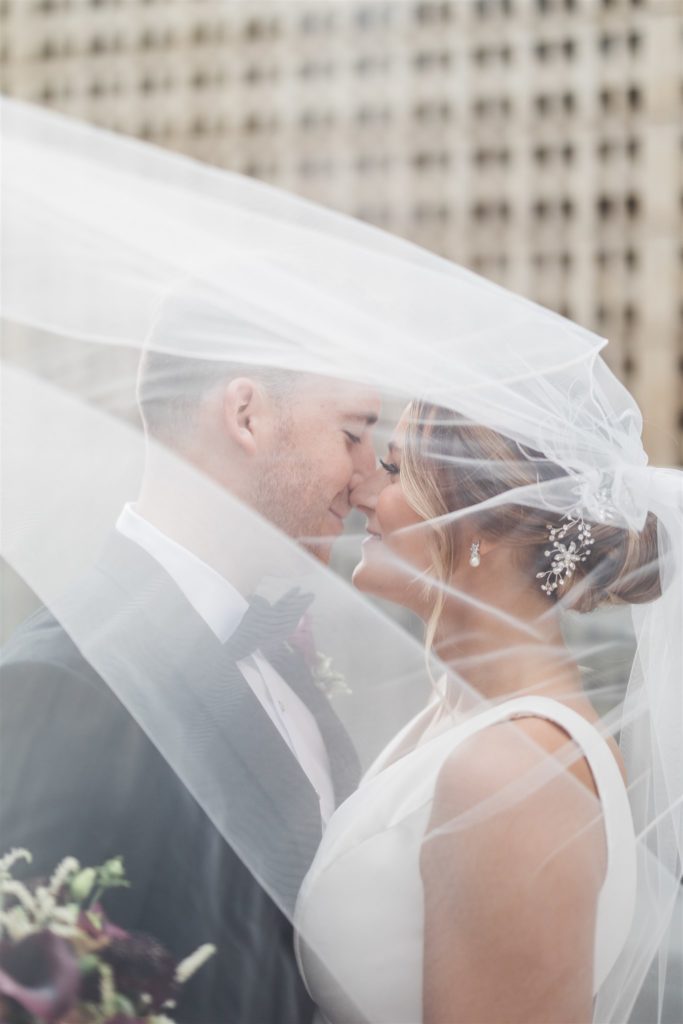 Bride and groom under veil together smiling 