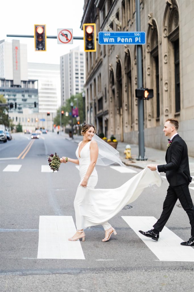 Groom carries brides gown as they cross the street in downtown Pittsburgh