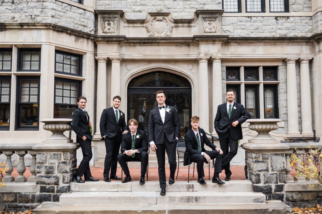 Groom poses with groomsmen in front of the Mansions on Fifth