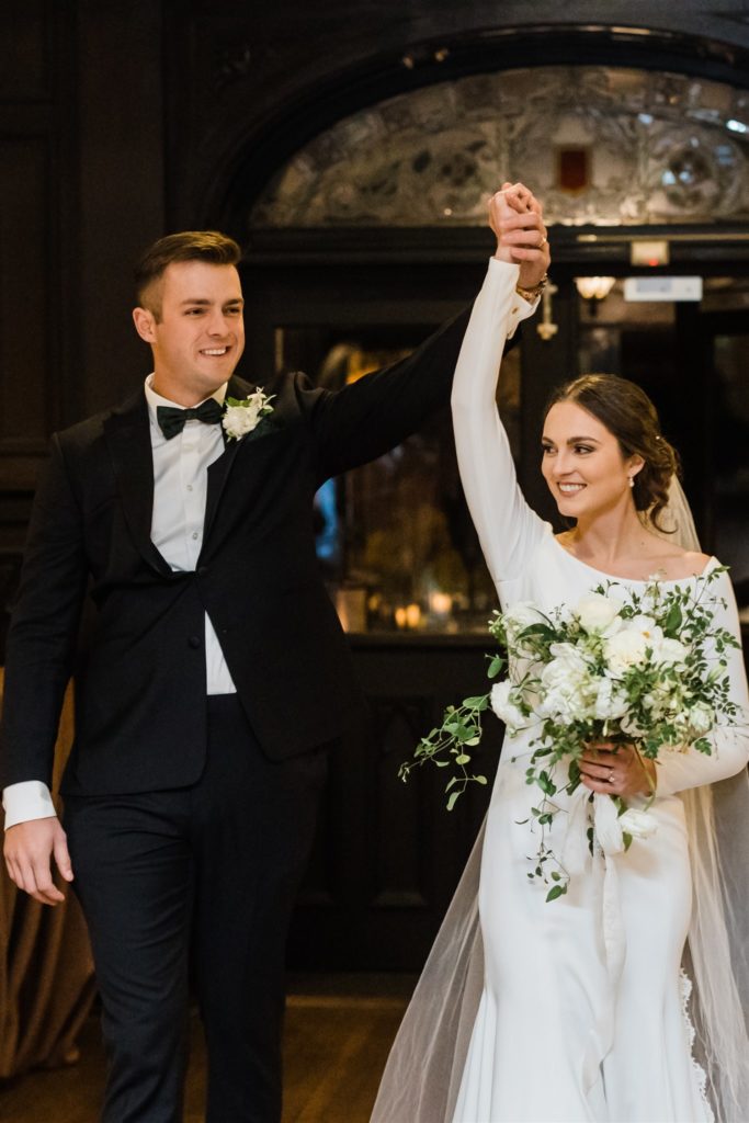 Bride and groom raise their hands as they enter their Mansions on Fifth wedding 