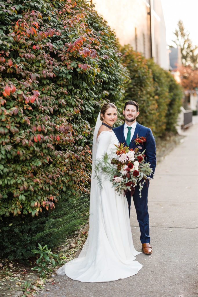 Bride and groom pose together against wall of fall greenery