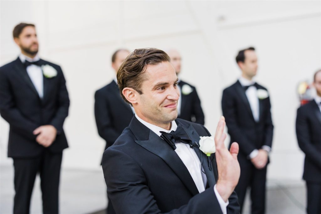 Groom waves as he sees the bride at the end of the aisle