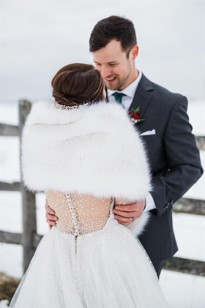 Groom warms the arms of bride as they pose outside a wintery background
