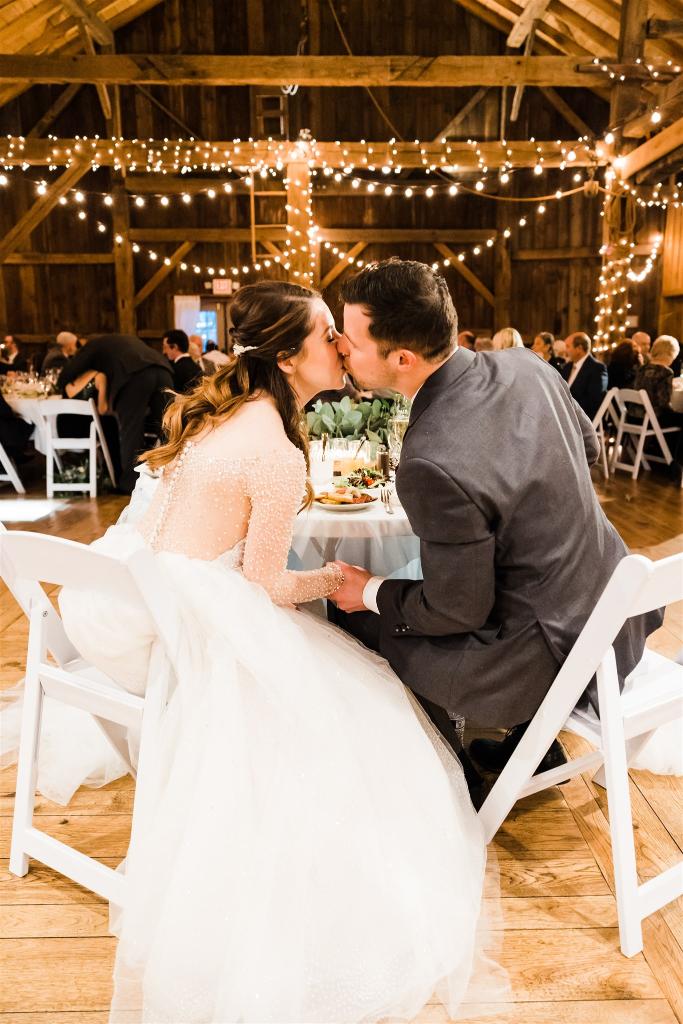 Bride and groom kiss at sweetheart table at Armstrong Farms Winter Wedding