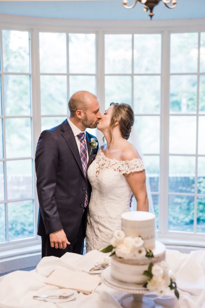 Bride and groom kiss in front of wedding cake at Wedding at Succop Conservancy