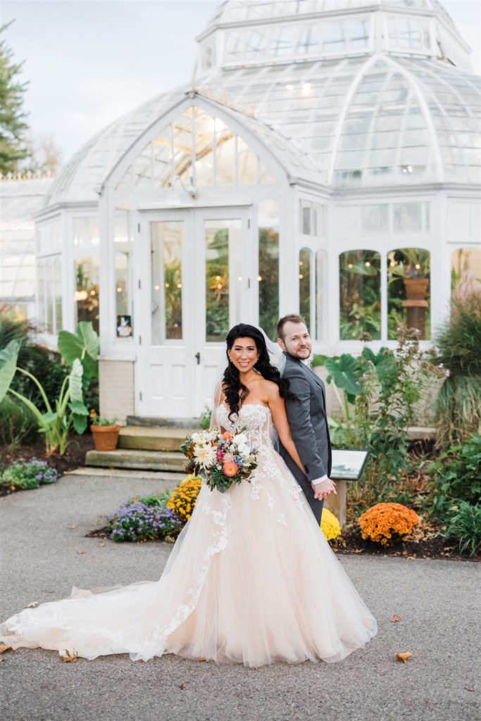 bride and groom stand in front of the greenhouse at their Fall Frick Pittsburgh Wedding 